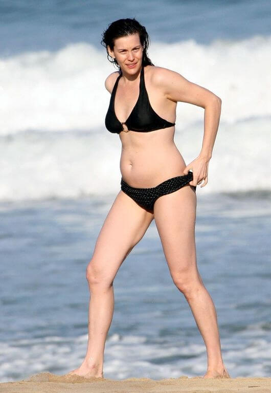 Med henne smal kropp och Mörk brun hårtyp utan behå (kupstorlek 36B) på stranden i bikini
