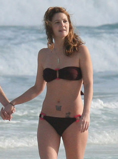 Con il suo snella corpo e Marrone chiaro tipo di capelli senza reggiseno (dimensione coppa 34C) sulla spiaggia in bikini
