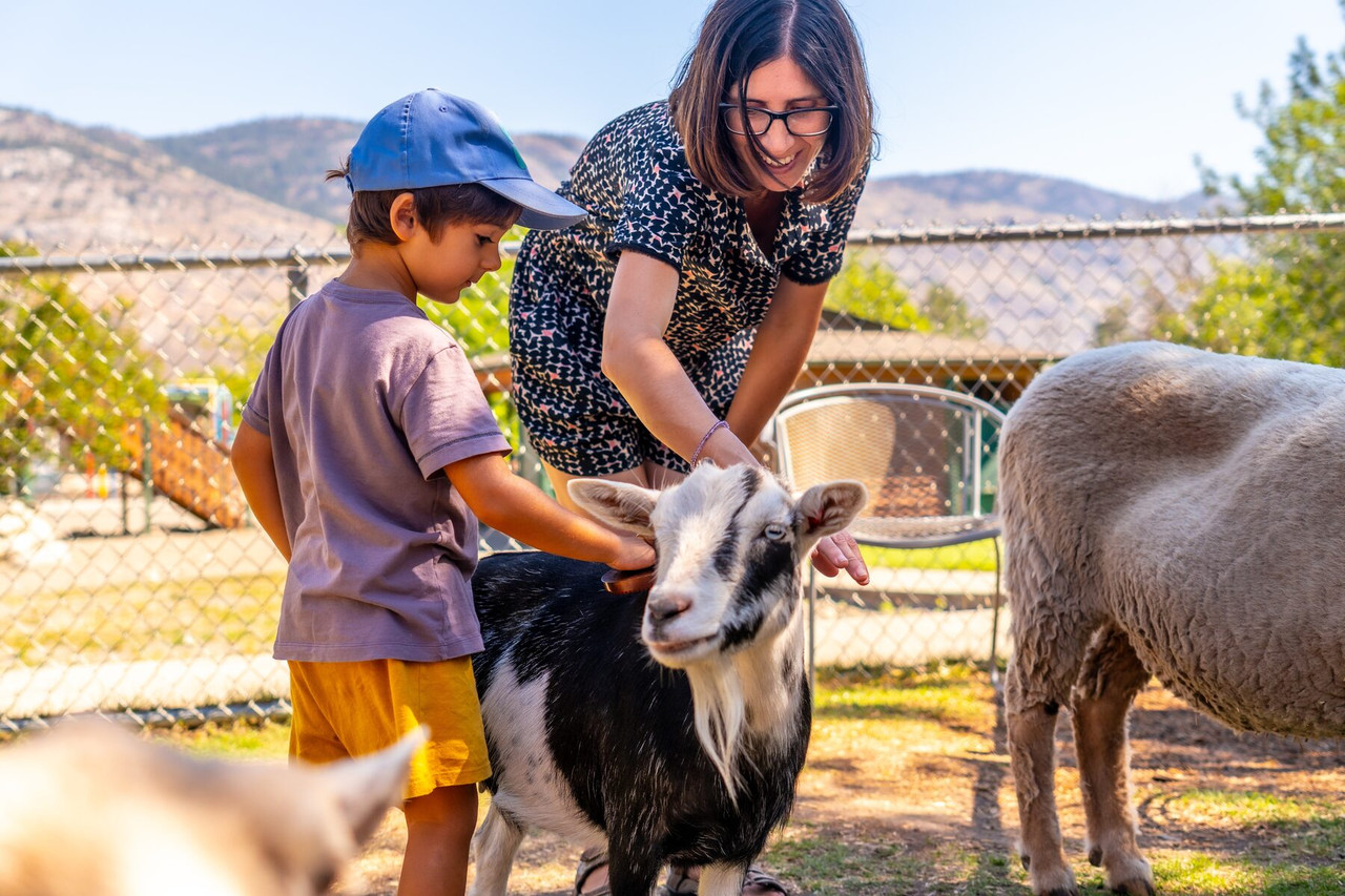 A mother and young son pet a goat at a small farm.