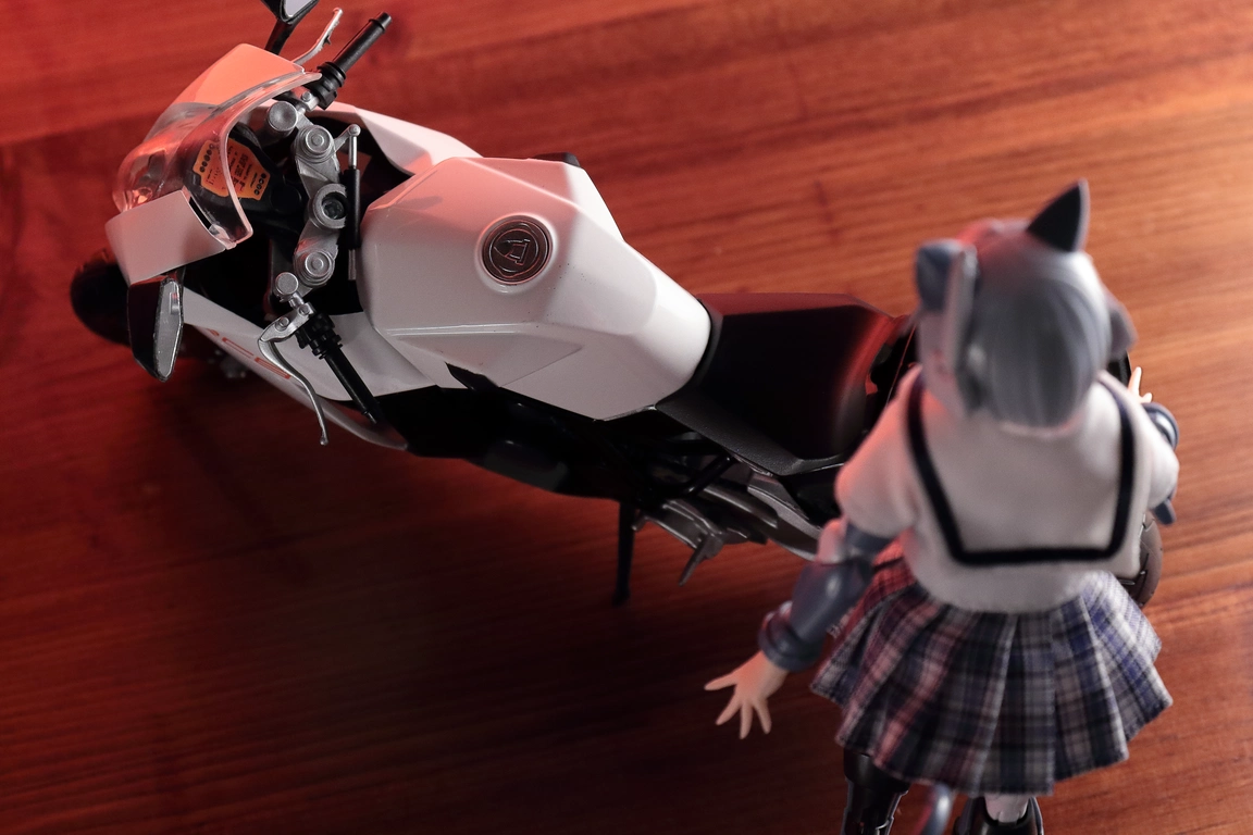 A top view of a 1:12 scale diecast model of the RC8 in white and “Variable Fighter Girls” Kairos girl wearing a 1/12 White Collar Check Sailor Uniform Set in blue