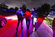 Federal agents wearing POLICE ICE and FBI vests escorting a handcuffed man during a nighttime ICE enforcement operation