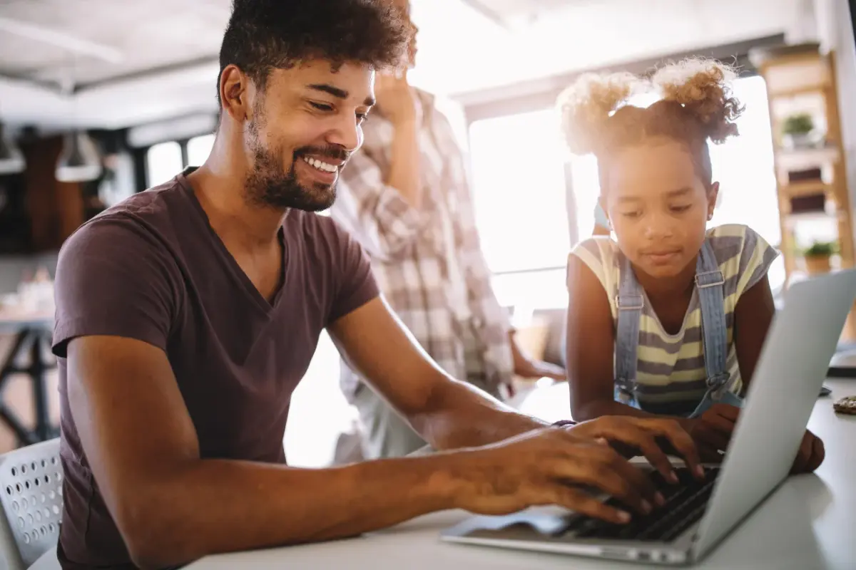 father and child looking at each other smiling while on laptop