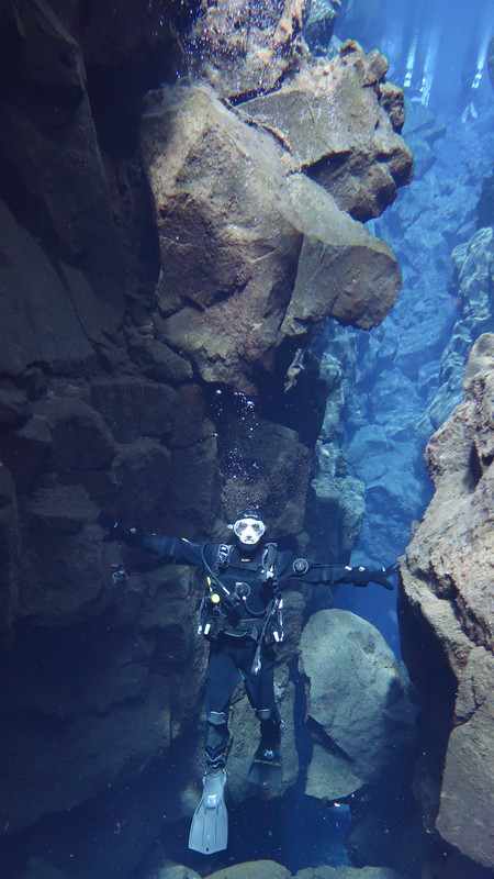 A diver with arms outstretched in the Silfra fissure, Iceland, touching the North American and European plates