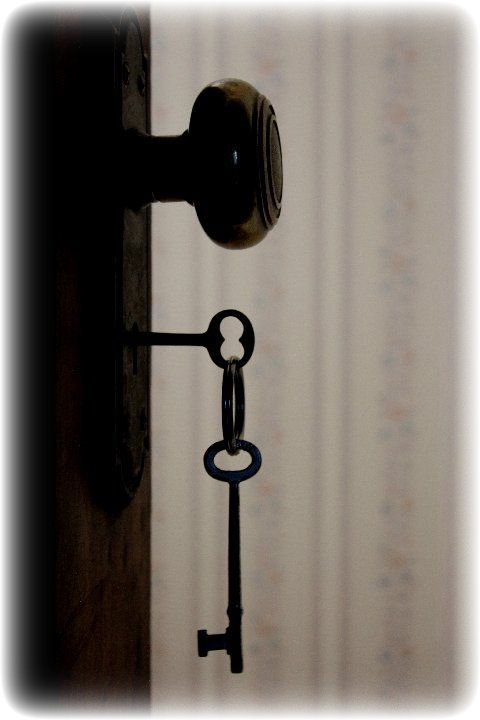 a vintage key sticking out of a lock in a door, with a keyring with another key hanging off of it. the background is blurry, but is clearly vintage wallpaper. the edges of the image are blurred out.