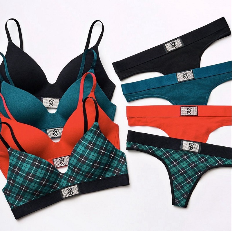 Раскладка комплектов белья на белом фоне: бюстгальтеры и стринги в чёрном, бирюзовом и красном цветах, а также в зелёную клетку, с декоративной эмблемой на поясе.