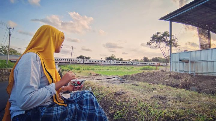 Pelanggan Mie Ayam Pakde Wonogiri sedang menyantap makanan sambil melihat perjalanan kereta api.