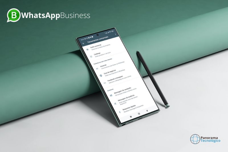Smartphone escorado em uma bobina de papel azul mostrando as ferramentas comerciais do WhatsApp Business com uma caneta ao lado e em cima de uma mesa branca.
