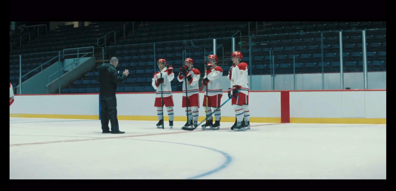 4 team russia youth national hockey team stand near center ice receiving notes from their coach. their uniforms are white, red, gold, and blue. their jerseys have a white base, gold lettering, red shoulders and cuffs, and 2 stripes, one white and one blue, at the hips. their shorts are red with white and blue vertical stripes on the side. they have white socks with a red and blue stripe near the knee. their helmets are red.