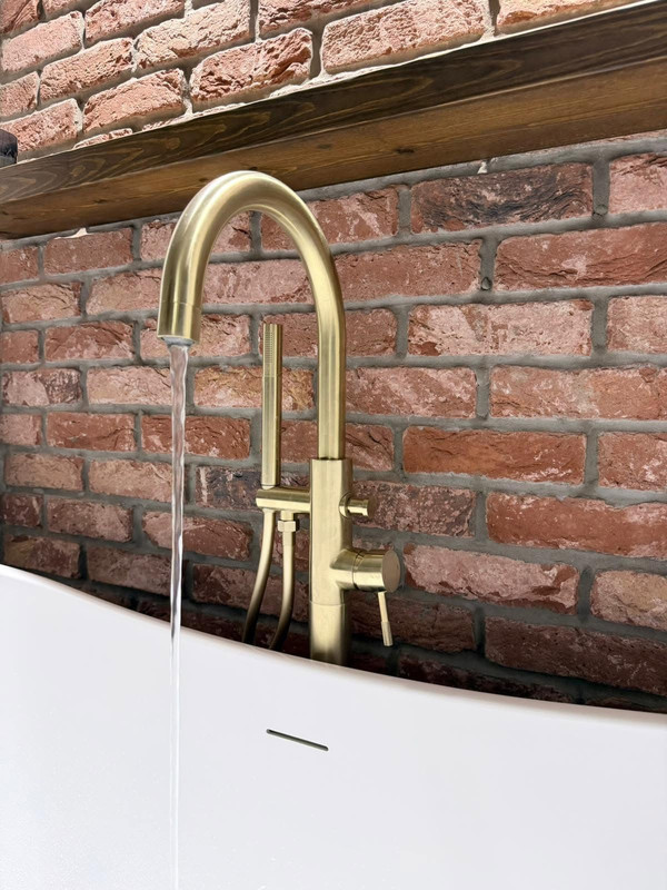 Close up brushed brass bath tap with exposed brick background