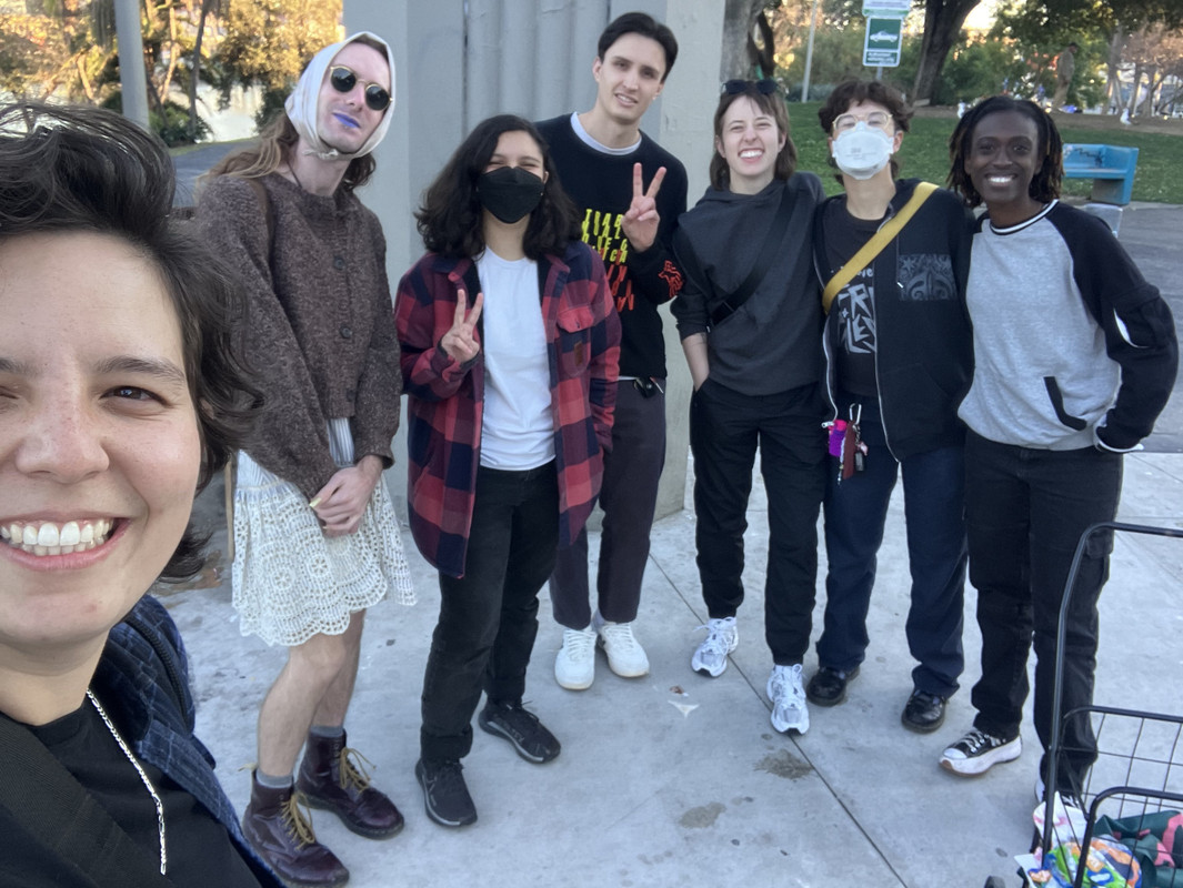 A group selfie of seven people standing together, celebrating a successful burrito distribution! Only one is not a dyke.