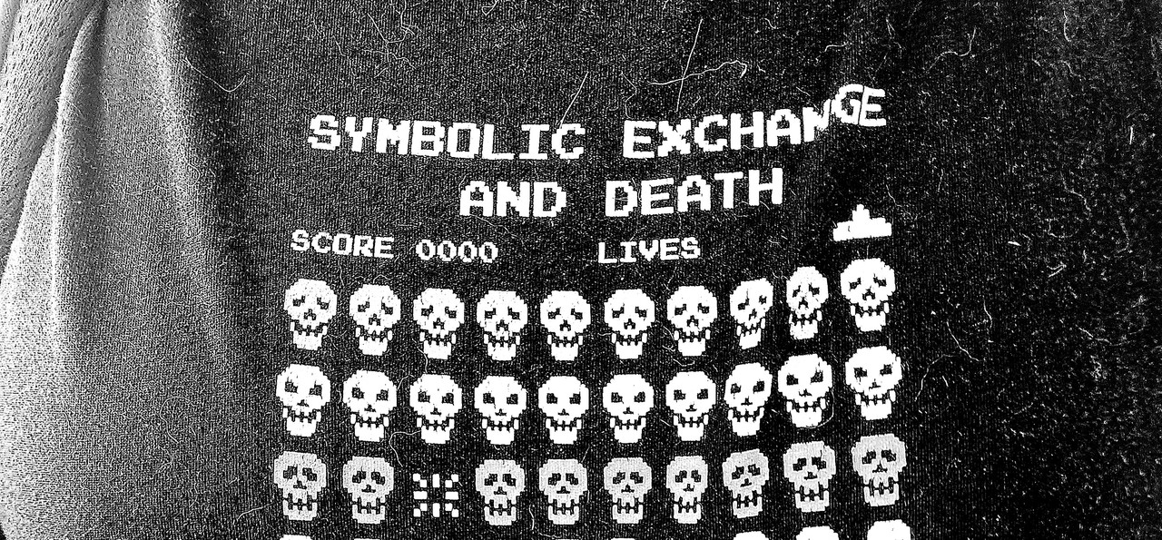 a t-shirt with _invaders_-style screenshot but the aliens are skulls. the text reads: "SYMBOLIC EXCHANGE AND DEATH; BY JEAN BAUDRILLARD"
