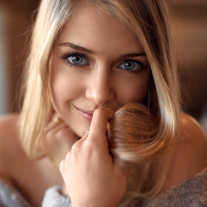 A girl with long blonde hair and blue eyes is looking directly at you with a ravishing gaze