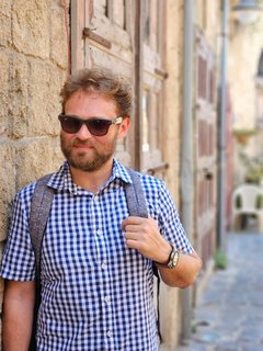 White male in sunglasses and blue button-up shirt leaning against a wall in an alleyway in Batroun, Lebanon