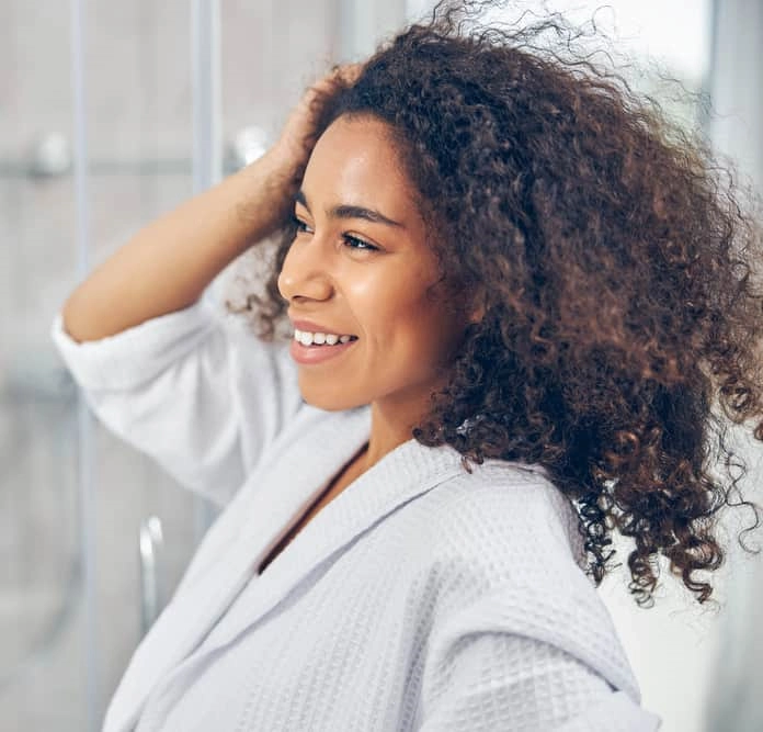 Smiling dark-skinned girl air-drying curly hair in bathroom