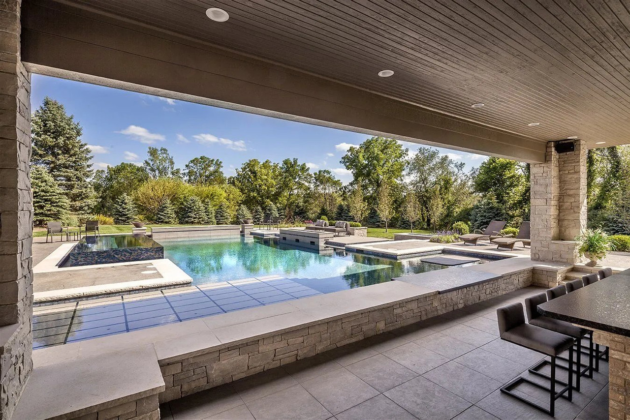 Covered outdoor dining area overlooking a landscaped pool and paved patio
