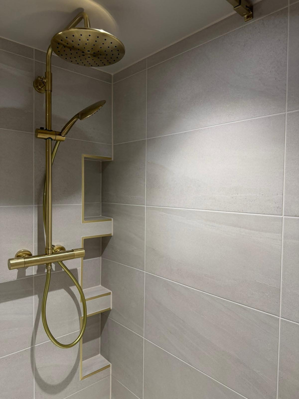 Brushed brass shower against soft neutral bathroom tiles