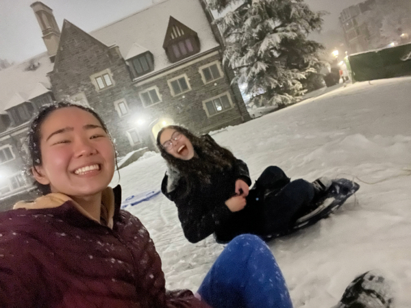 Two students smiling and sitting on two sleds