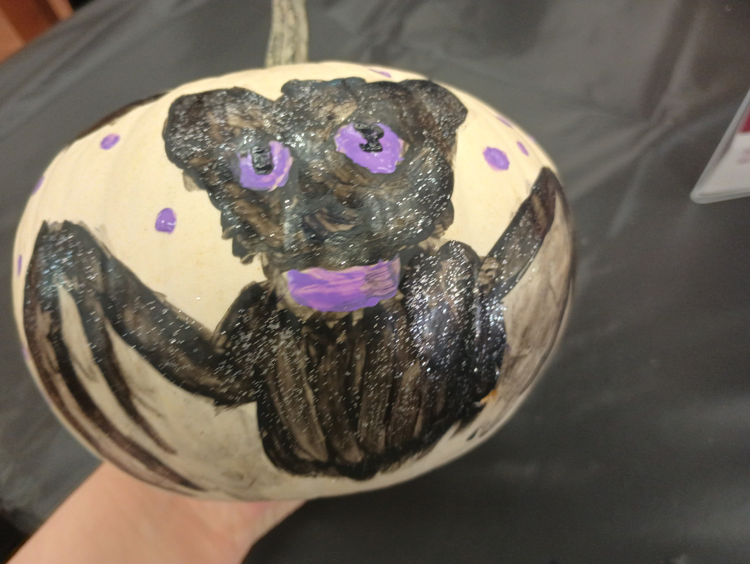 A black bat with purple eyes painted on a white pumpkin