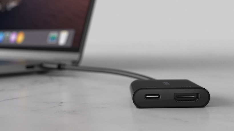 Adaptador Belkin conectado a una laptop y a un monitor, mostrando su función dual.