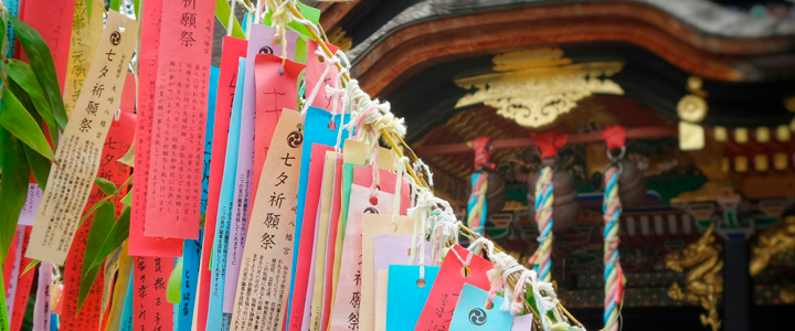 Foto de um templo japonês, com vários papéis retangulares pendurados no bambu, escritos com desejos do Tanabata. Por Franck V. no Unplash.