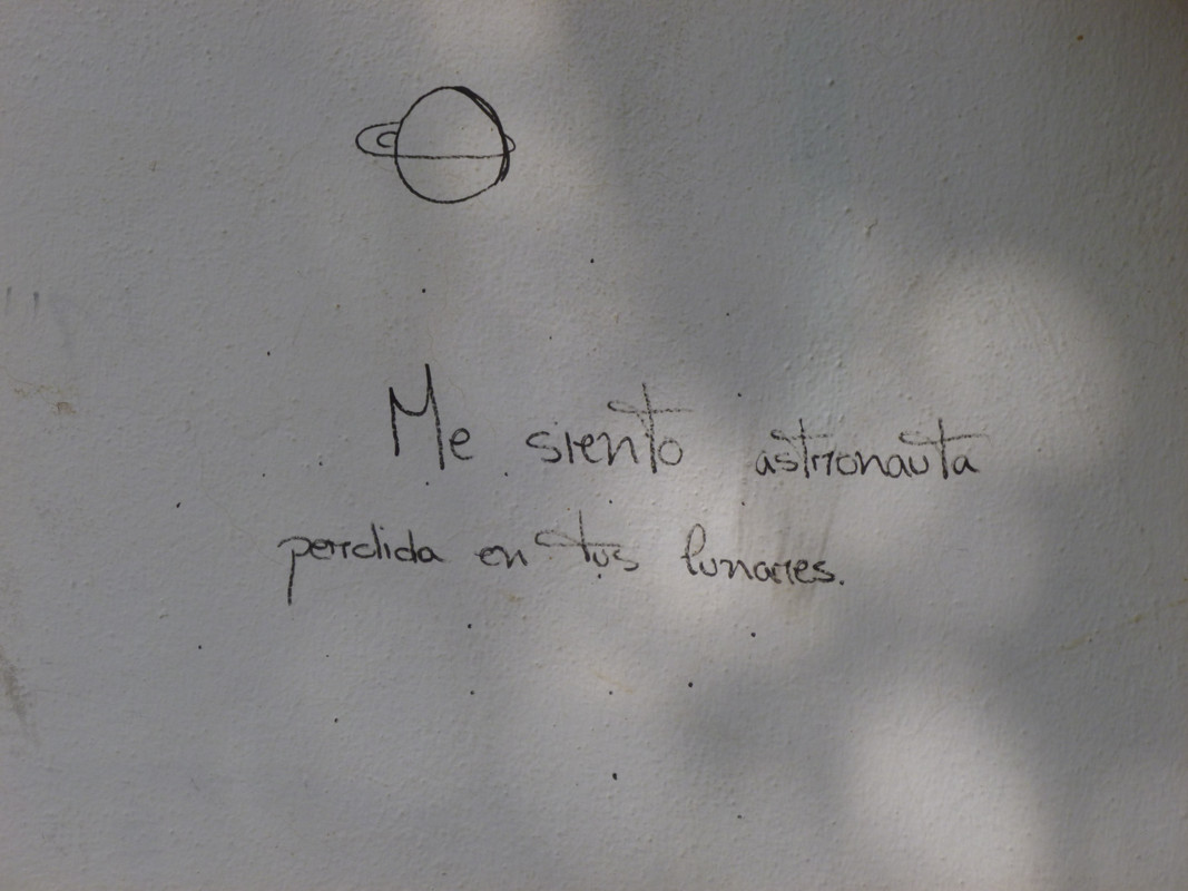 White wall, with a very basic drawing of a planet with something orbiting it.  Underneath is something that says something like Me siento astronauta pendida en los lunanes, which google translates as I feel like an astronaut hanging in the moon