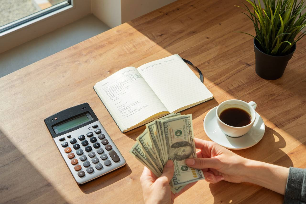 Budgeting with calculator, notebook, and cash on a wooden desk