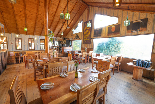 Comedor de Cervecería Rural con mesas de madera y grandes ventanales