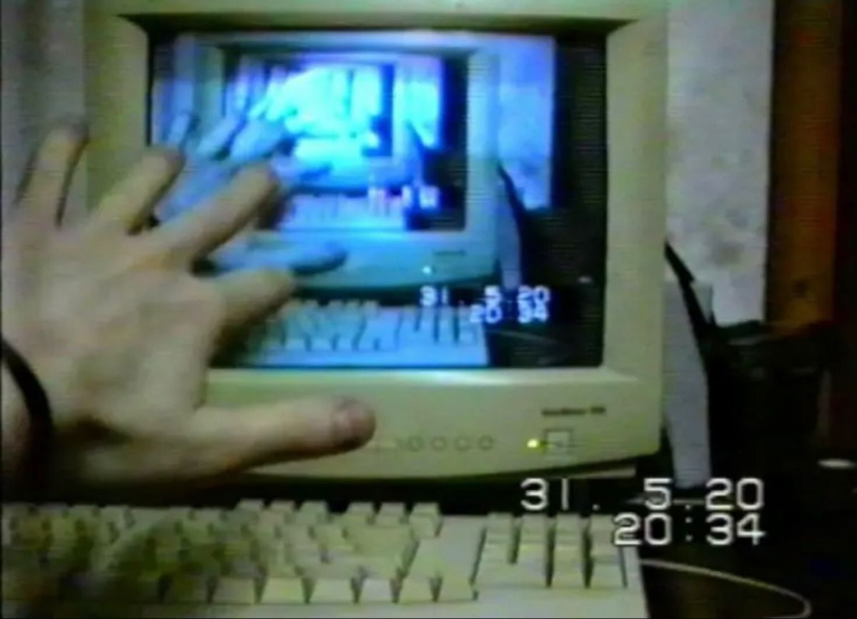 a grainy picture of a computer with a blue screen, with a hand reaching towards it