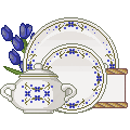 White plate with blue flowers, a teapot and blue tulips in the back.