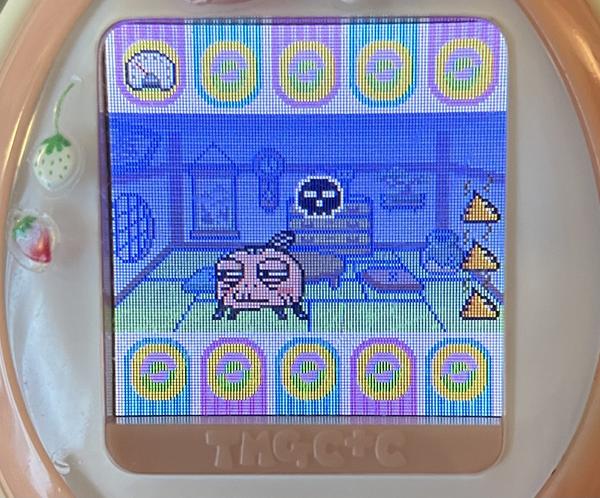 a close up photograph of my tamagotchi device showing a tama that looks like an old woman, unhappy and sick next to a pile of her own feces. but in a cute and cartoony style