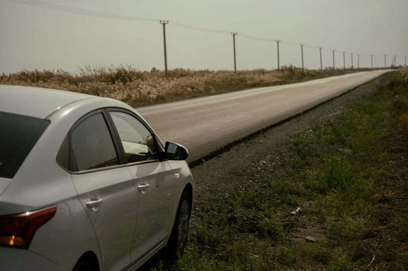 silver car parked on the side of a long rural road