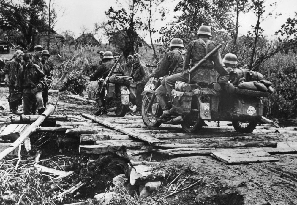 Kradschützen einer Aufklärungsabteilung der Waffen-SS passieren auf dem Vormarsch eine behelsfmäßige