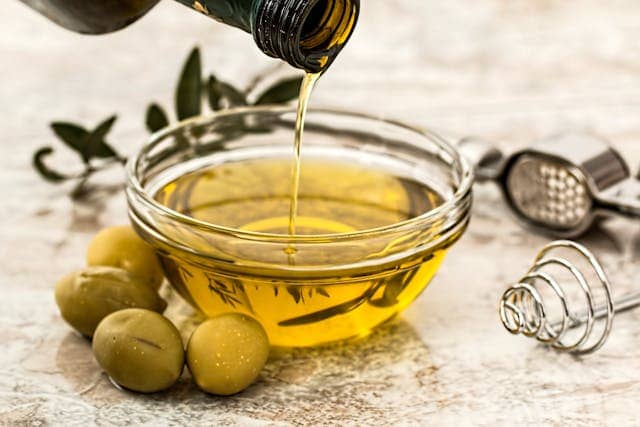 A bottle of Extra virgin olive oil pouring in a bowl with some olives beside the bowl
