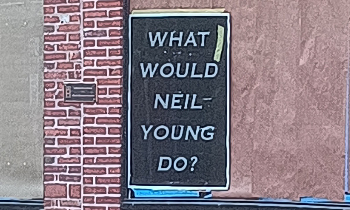 A poster on a building that says, "WHAT WOULD NEIL YOUNG DO?"