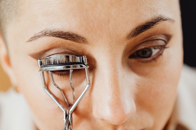 a woman curling her eyelashes with eyelash curler before applying mascara 