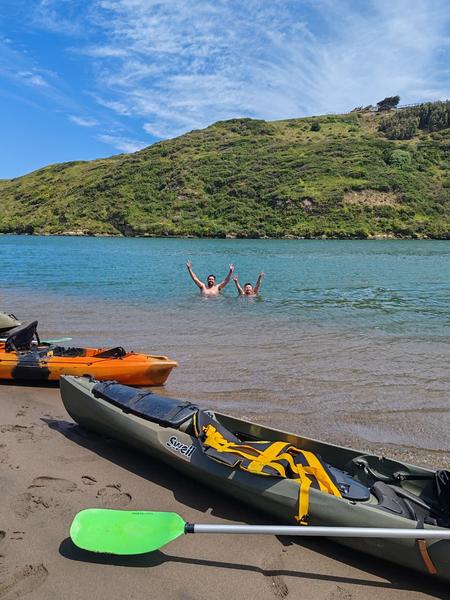 Kayaks en la orilla del río Rapel con bañistas al fondo