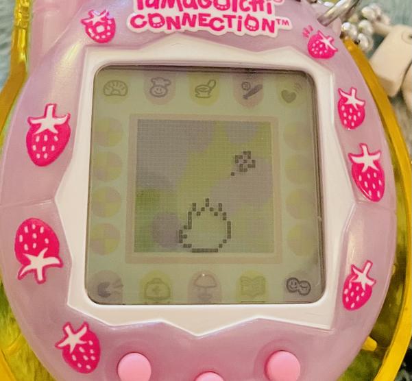 up close photo of a tamagotchi connection device (2024 rerelease) showing alibi as a teenager facing away from the screen and pouting