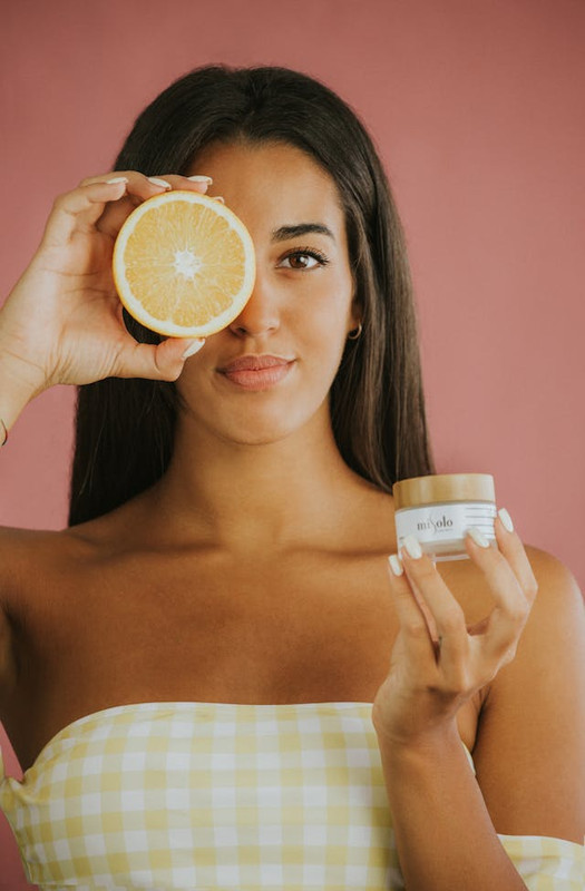Woman holding vitamin C cream and an orange showing how vitamin C supports healthy, bright skin.