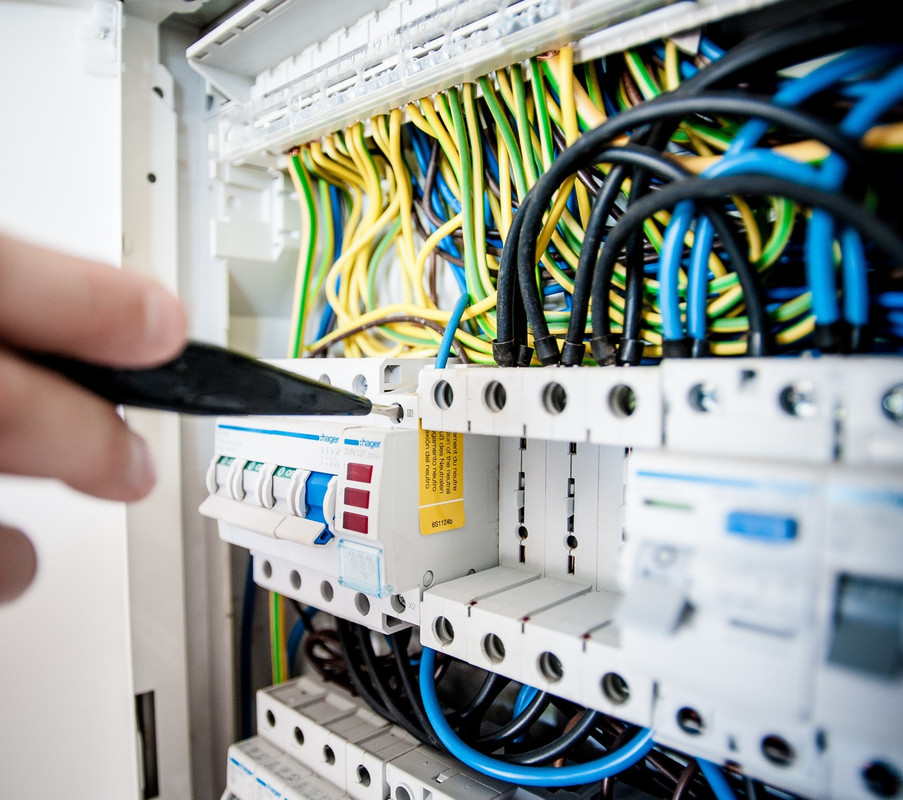 hand with tool working on panel with several colorful electrical wires