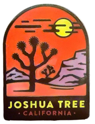 an enamel pin of a black silhouette joshua tree in a desert, in front of a red sky and mountains, that says 'Joshua Tree California' at the bottom