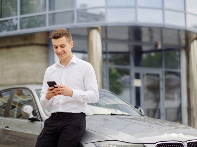man checking vehicle information on his phone while inspecting a used car before purchase
