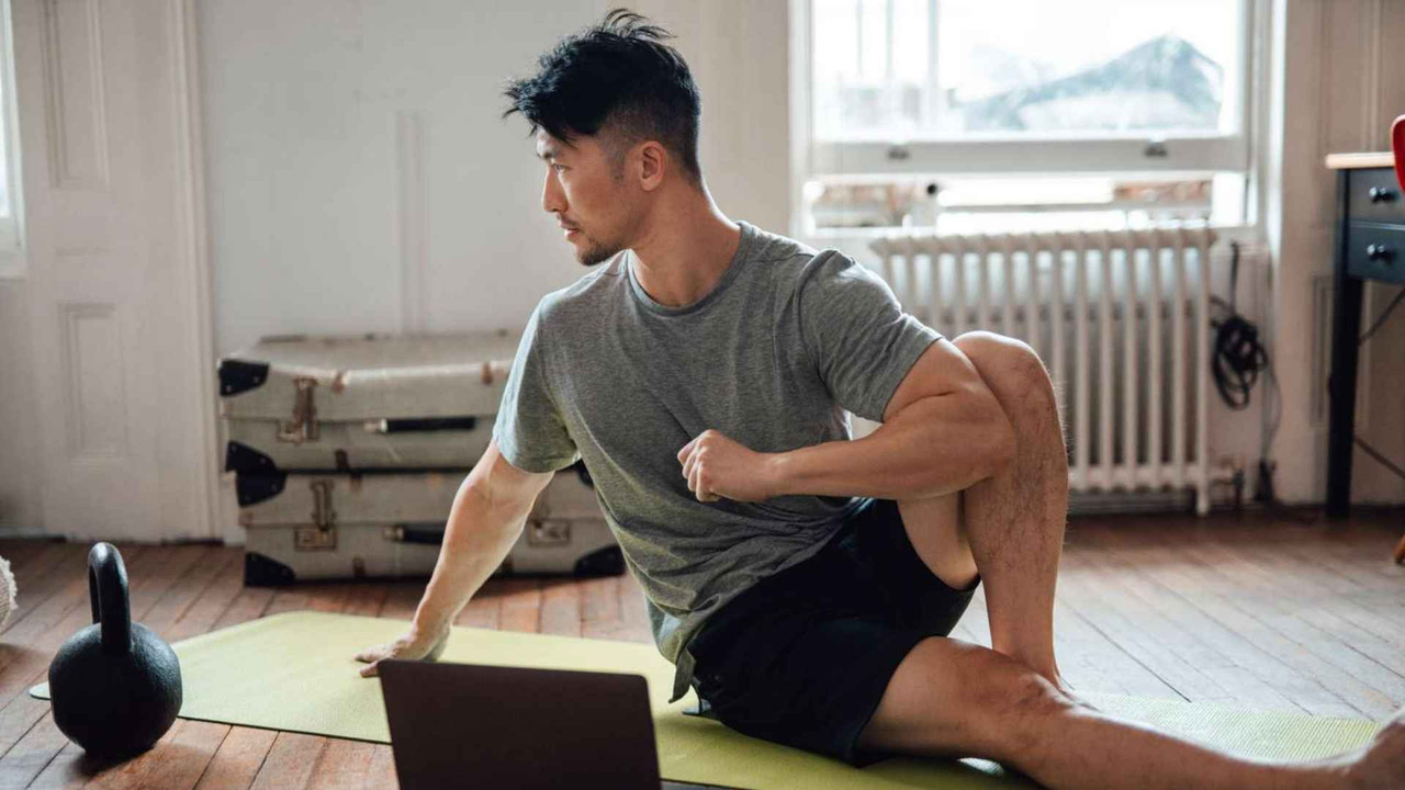 Nam giới tranh thủ kéo giãn lưng xoay thân bên cạnh laptop và kettlebell tại nhà