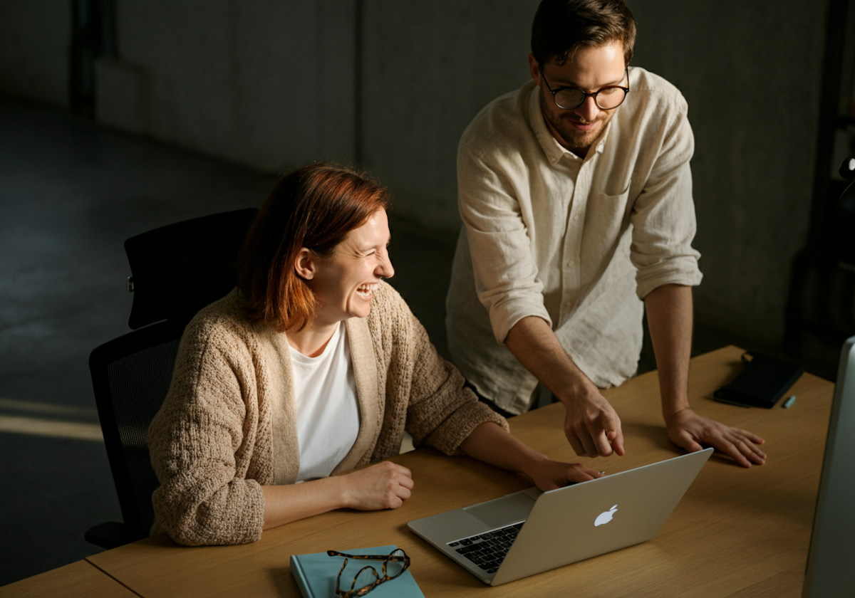 Två kollegor som samarbetar vid en laptop i ett ljust, modernt kontorslandskap.