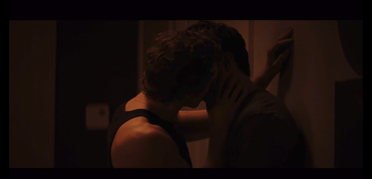 ilya kissing shane up against a wall. ilya's wearing a black tank top and ilya is in a gray t-shirt.