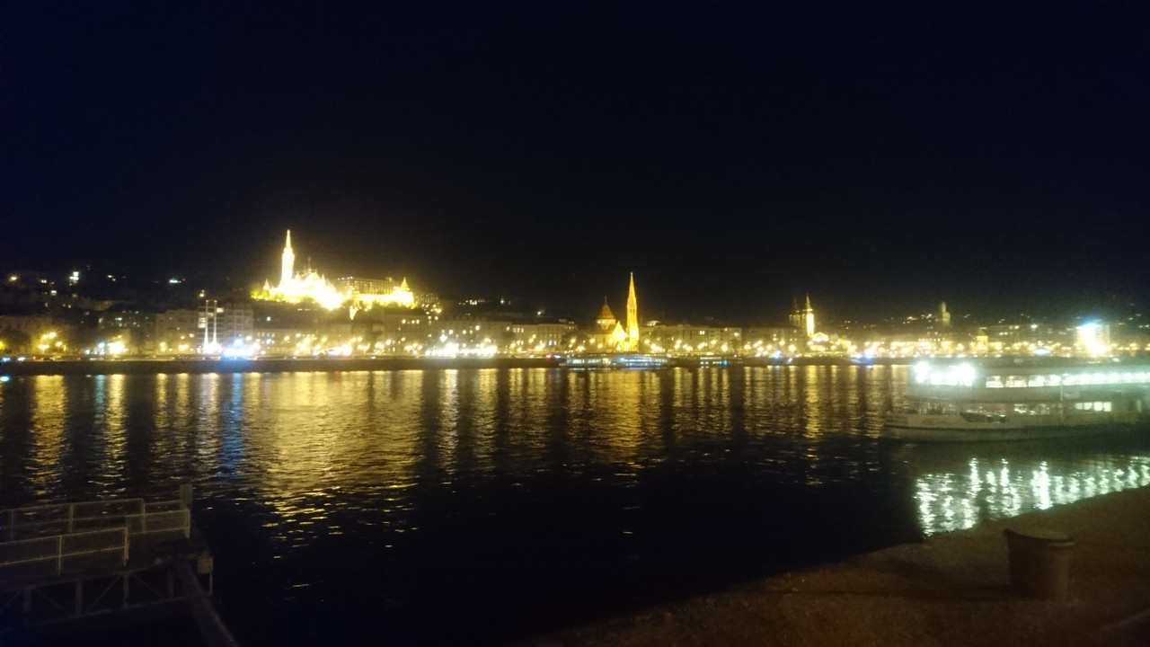 Budapest castle at night. It is illuminated, and stands above the rest of the riverside, which is also illuminated.