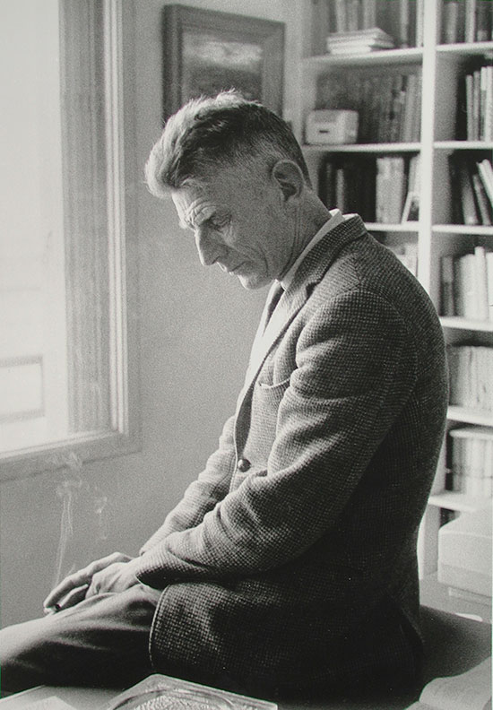 Samuel-Beckett-profile-view-sitting-on-a-table-Paris-1964