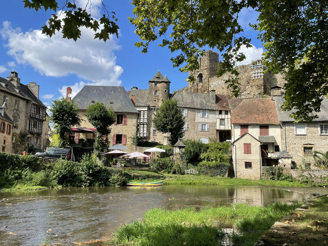 A photo of a river with stone houses, and a castle, on the background. The village is Ségur-le-Château.