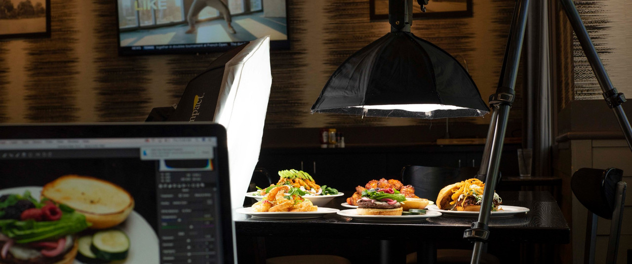 Behind the scenes restaurant food photography setup with lighting, camera tethering, and dishes ready for a shoot