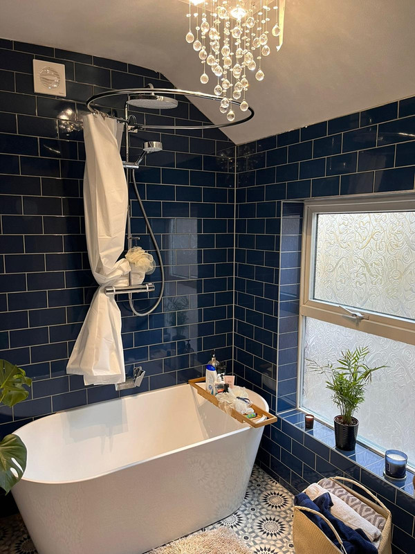 Luxury bathroom renovation with navy tiles, freestanding bath and chandelier