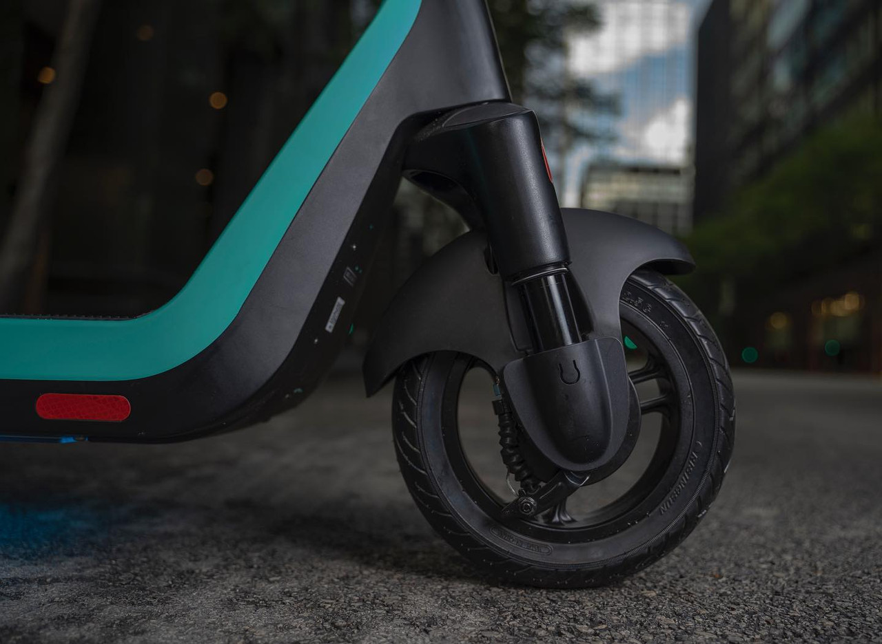 Close-up product detail photography of an electric scooter wheel and teal frame